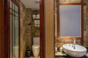 A bathroom with a stone wall, a white toilet, a sink with a mirror, and a towel rack. - Jinyatai Holiday Manor (Hengyang)