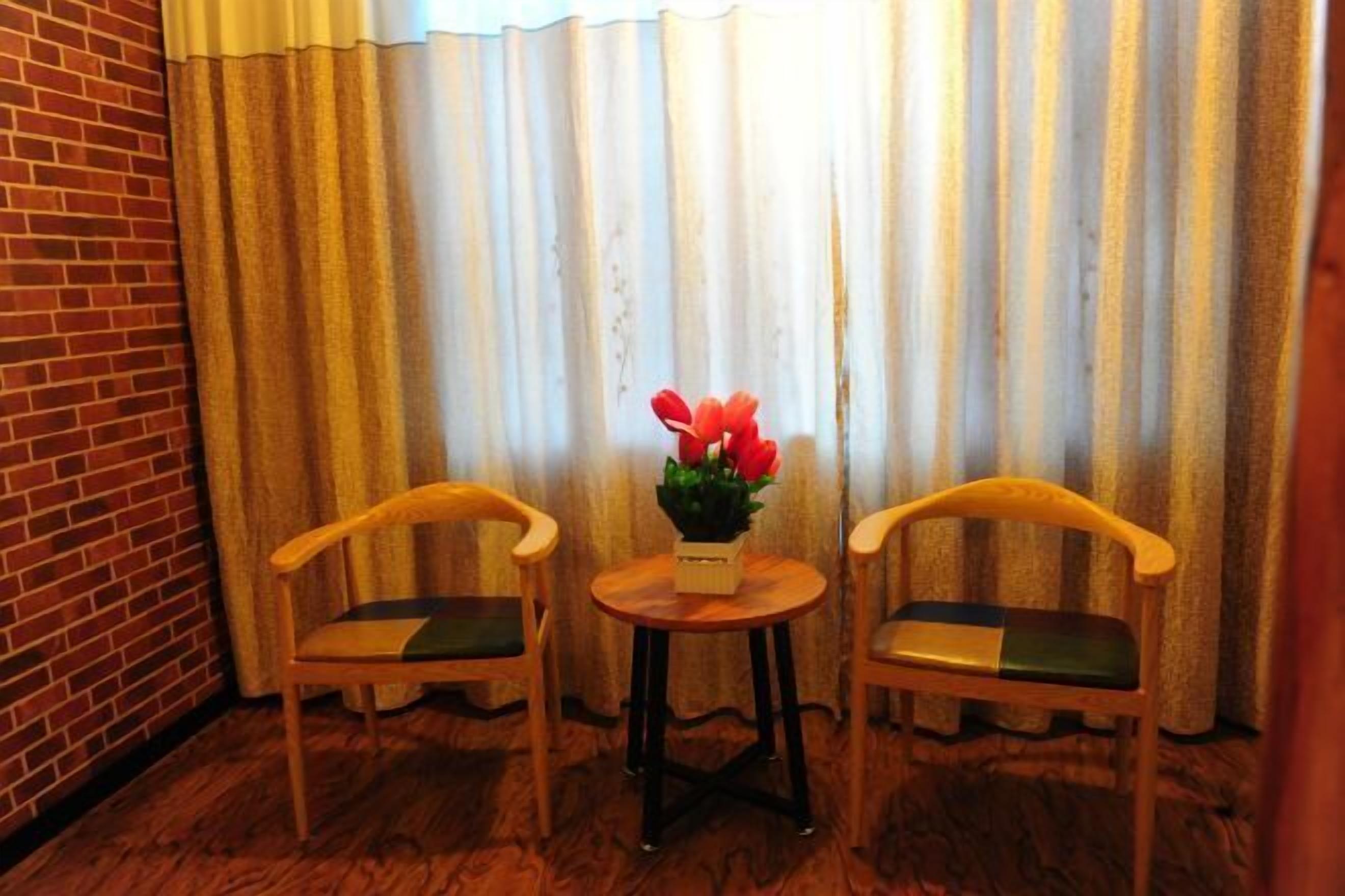 Une pièce comprenant deux chaises en bois, une petite table ronde et une plante en pot ornée de fleurs rouges.