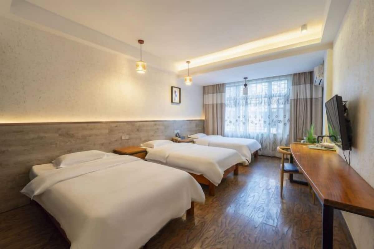 A hotel room with three beds, a wooden floor, a desk, and a TV.