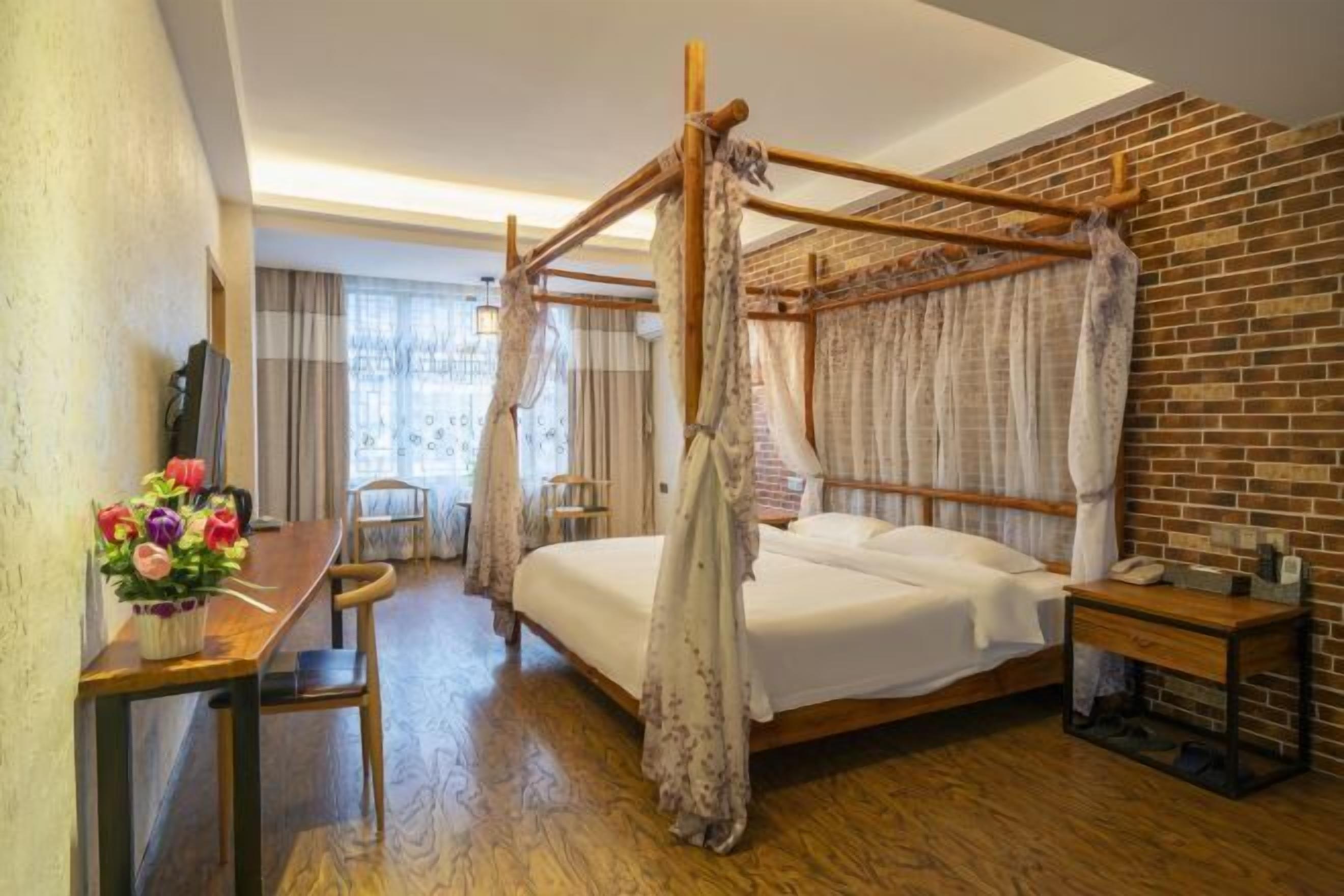 Una habitación con cama con dosel, un escritorio de madera con un jarrón de flores, una silla y una mesita de noche con lámpara.