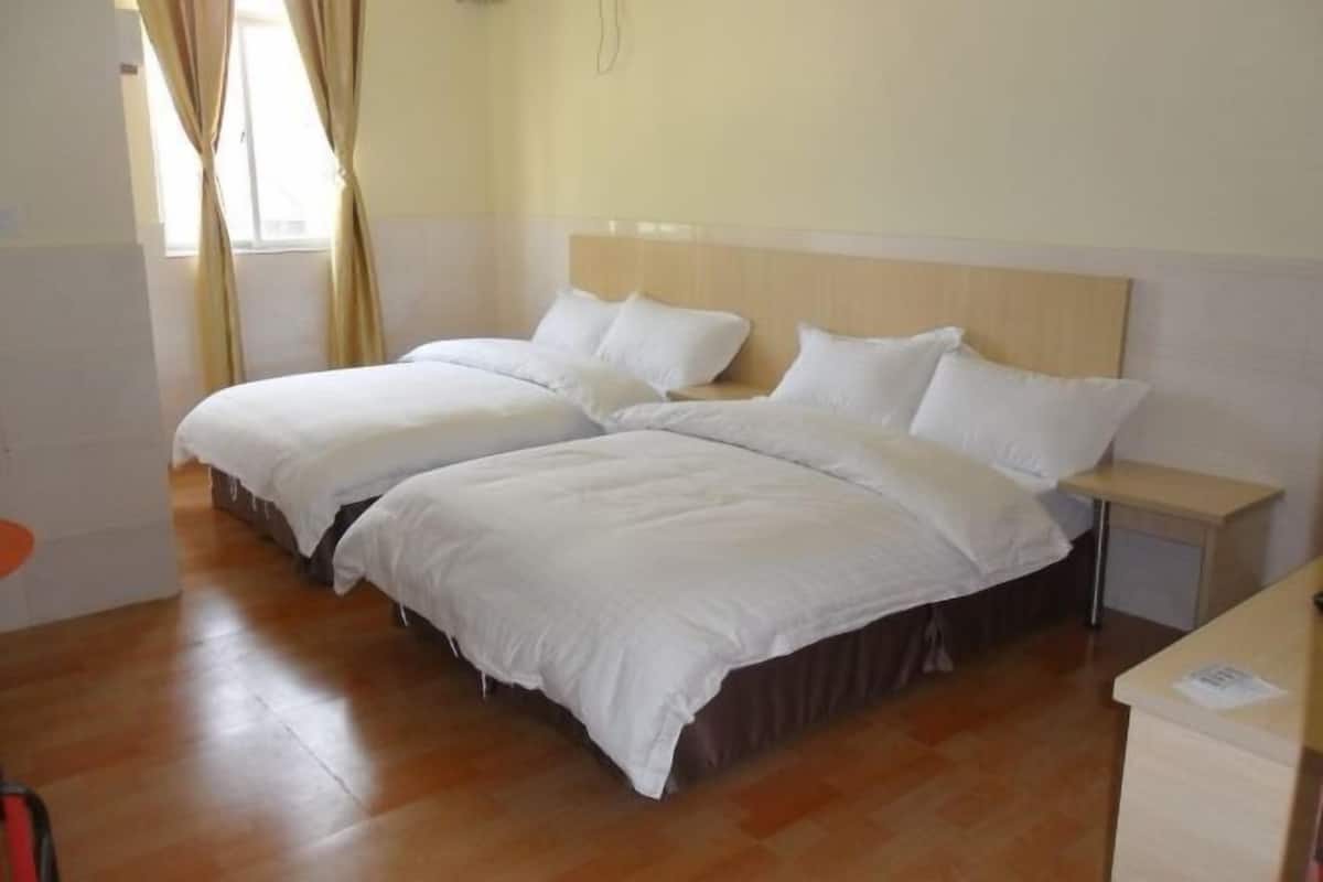 A hotel room with two beds, a wooden headboard, a bedside table, and a window with curtains.