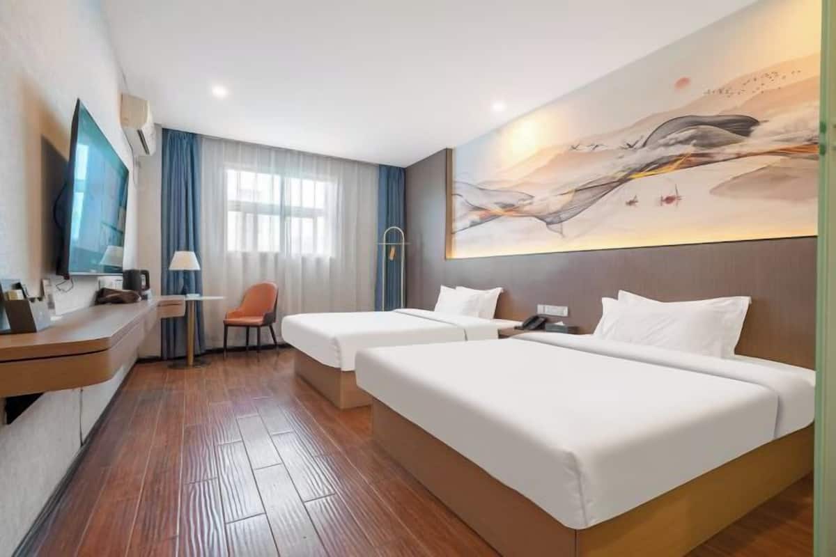 A hotel room with two beds, a desk, a chair, a TV, and a large abstract painting on the wall.