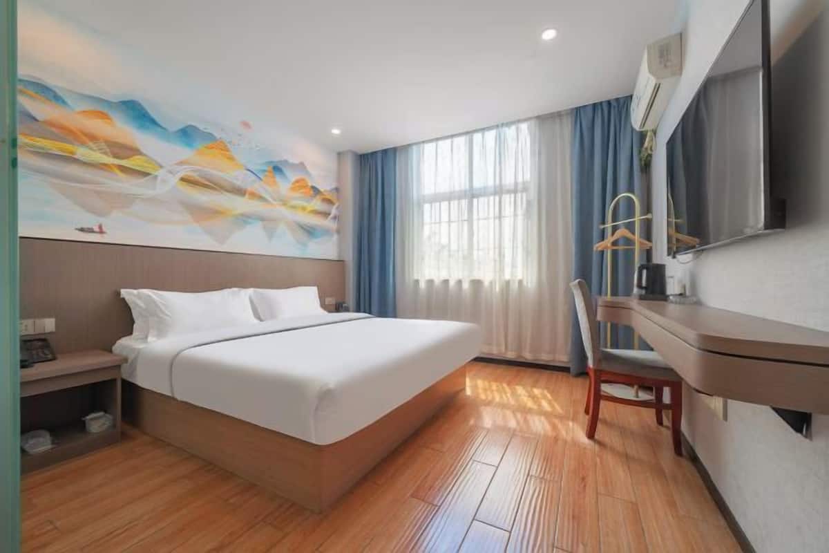 A modern hotel room with a large bed, a desk, and a painting on the wall.