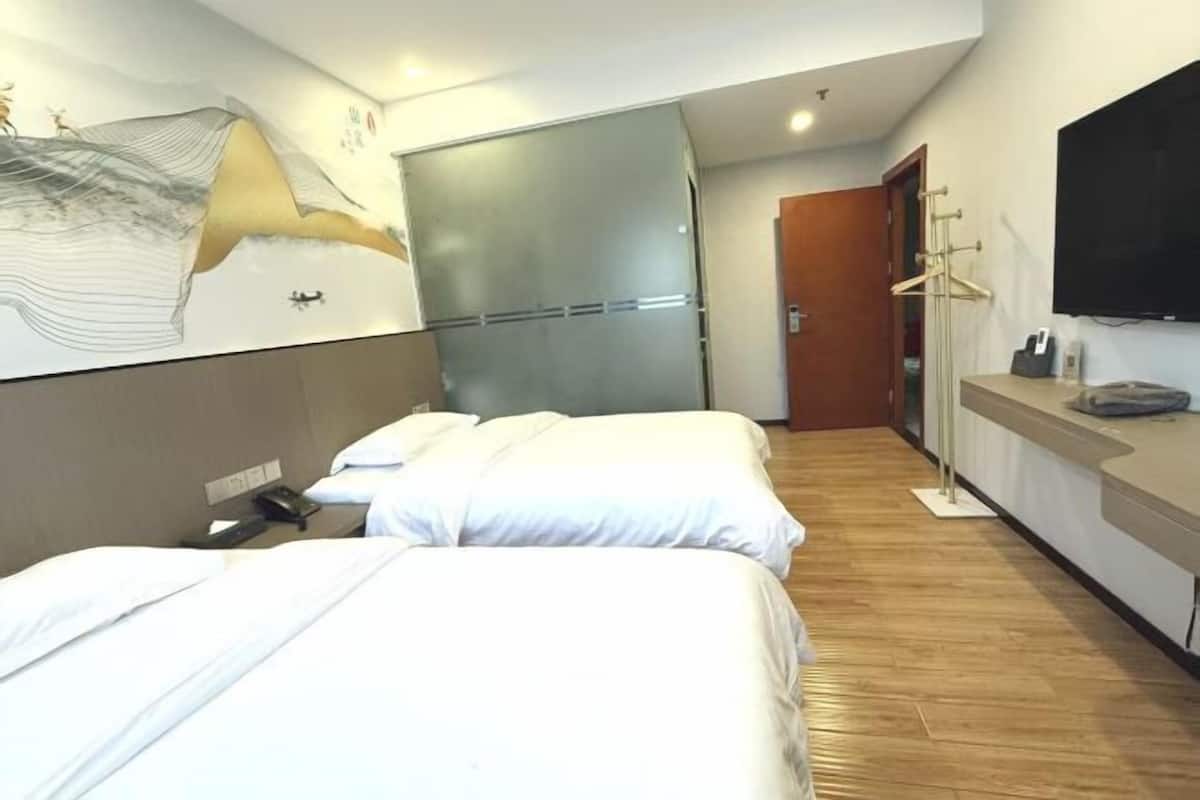 A hotel room with two beds, a flat-screen TV, a wooden floor, and a wall-mounted artwork.
