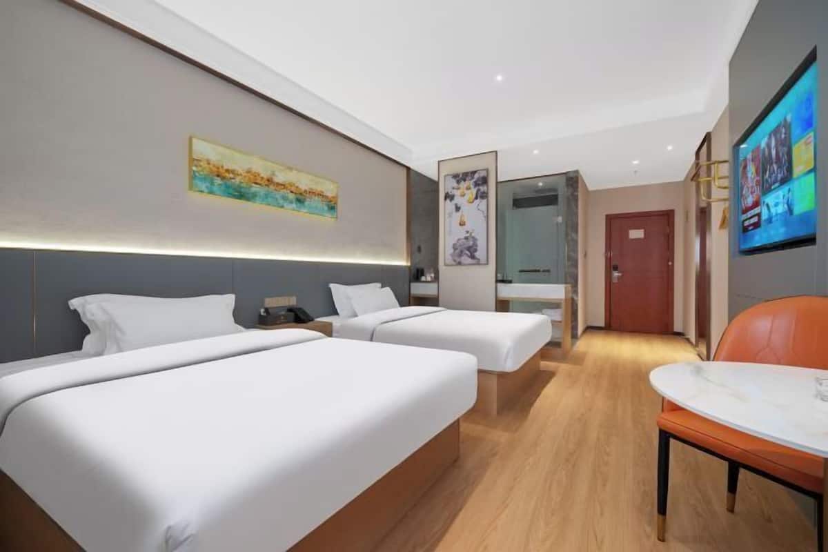 A hotel room with two beds, a desk, a chair, and a TV on the wall.