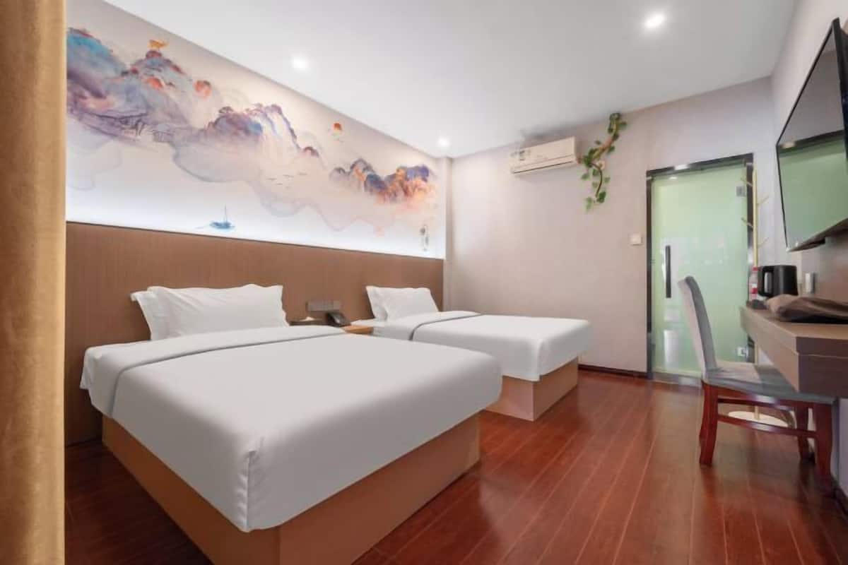 A hotel room with two beds, a desk, a chair, a TV, and a wall with abstract art.