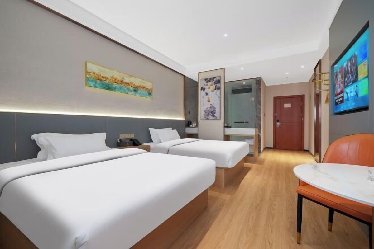 A hotel room with two beds, a desk, a chair, and a TV mounted on the wall.