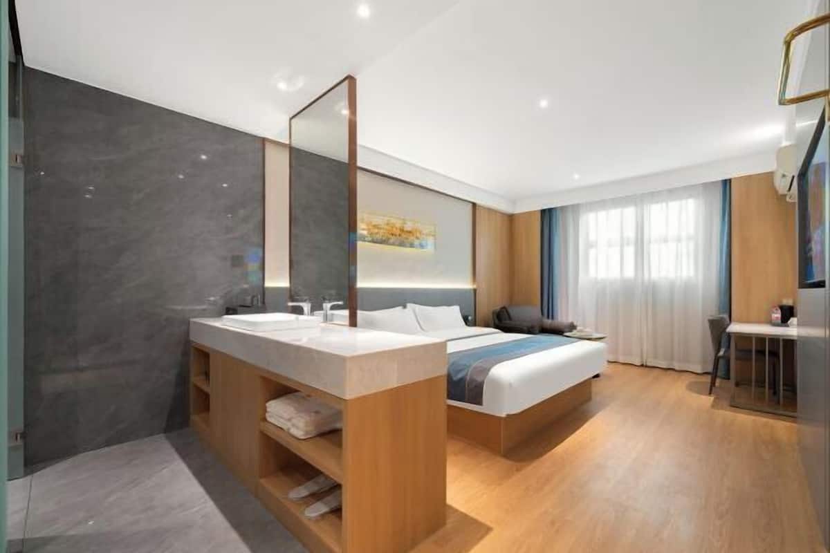 A modern hotel room with a large bed, a vanity with a mirror, and a separate seating area.