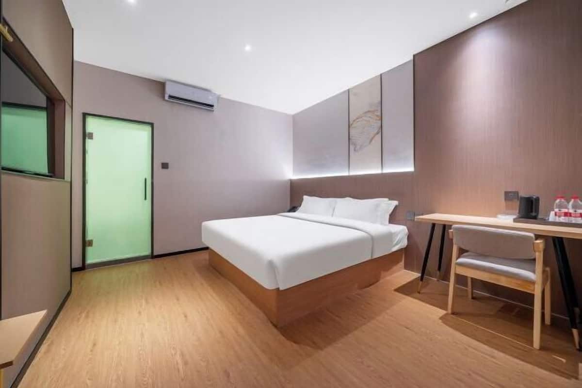 A modern hotel room with a bed, desk, chair, and a green door.