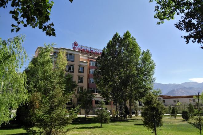 A multi-story hotel with a red sign, surrounded by trees and a clear sky.