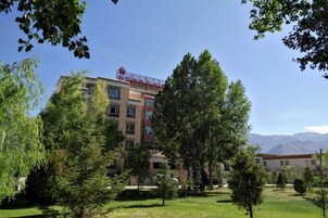 Un hotel de varios pisos con un letrero rojo, rodeado de árboles y un cielo despejado.