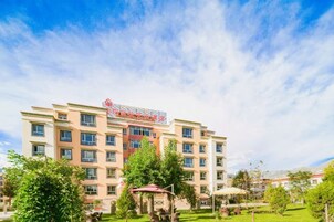 A multi-story hotel with a central entrance, surrounded by a well-maintained lawn and trees.