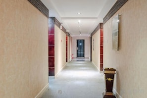A hallway with a carpeted floor, a door at the end, and a small table with a decorative item on the right. - Padma Chumig Garden Hotel (Lhasa)