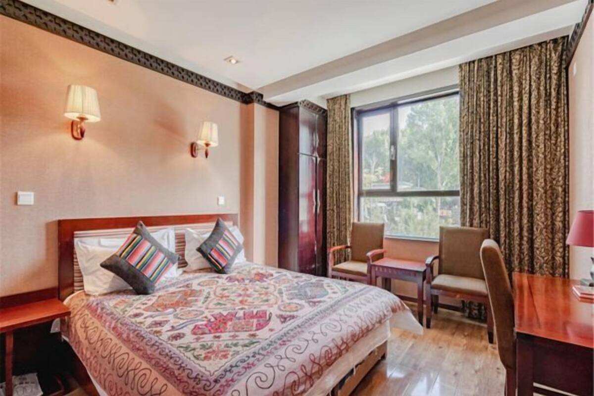 Een hotelkamer met een groot bed, twee wandlampen, een raam met gordijnen en een kleine tafel met stoelen.
