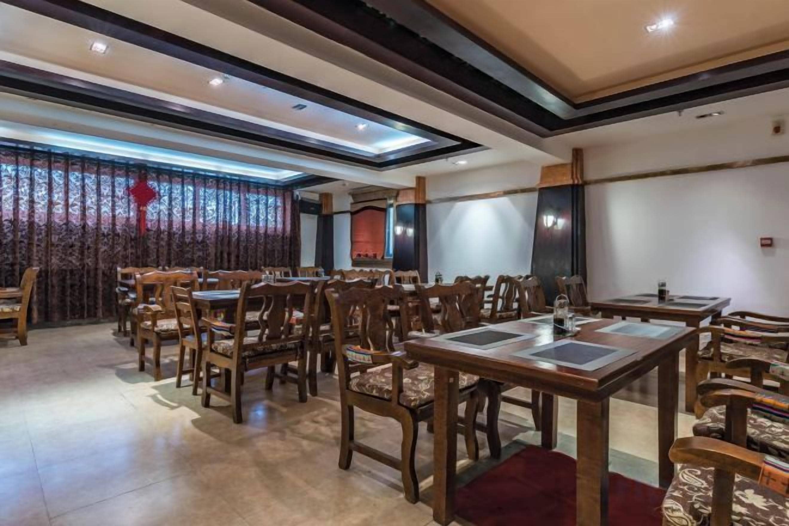 Restaurante com várias mesas e cadeiras, parede estampada e teto com iluminação embutida.