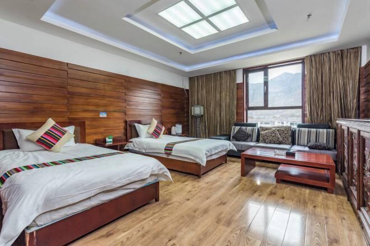 Een hotelkamer met twee bedden, een bank, een salontafel en een groot raam met uitzicht.