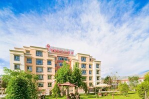 Hotel de diverses plantes amb un rètol destacat, envoltat de vegetació i un cel serè.