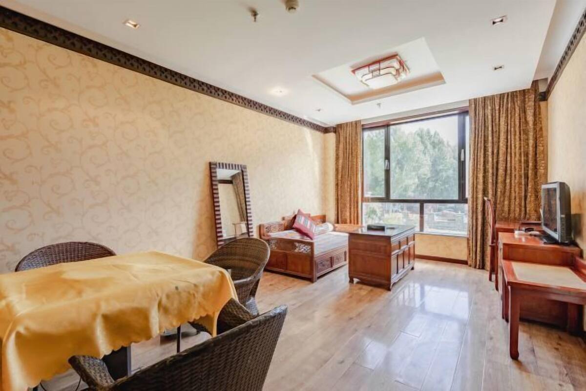 Hotelkamer met een bed, bureau, televisie, eettafel en een groot raam met gordijnen.