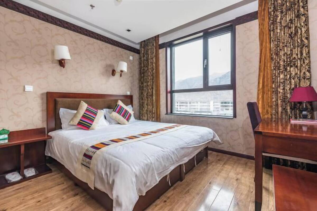 Hotelkamer met een groot bed, houten vloer, twee bedlampjes, een raam met uitzicht en een bureau met een lamp.