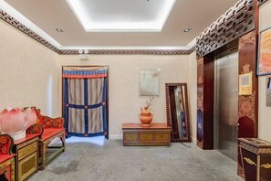 A room with a sofa, a small table, a decorative vase, a curtain, and an elevator. - Padma Chumig Garden Hotel (Lhasa)