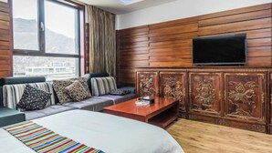 A hotel room with a large bed, a wooden panel wall, a television, and a sofa with cushions. - Padma Chumig Garden Hotel (Lhasa)