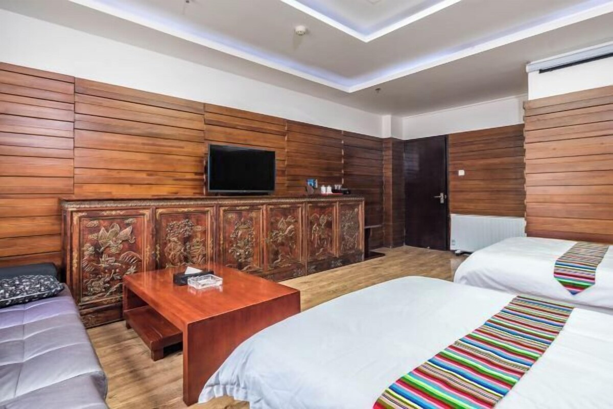 A hotel room with wooden paneling, a flat-screen TV, a wooden cabinet with carvings, a small table, two beds with striped bedspreads, and a door.