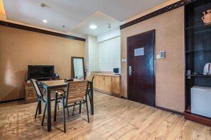 A hotel room with a wooden floor, a dining table with chairs, a television, a minibar, and a door with a small sign. - Padma Chumig Garden Hotel (Lhasa)