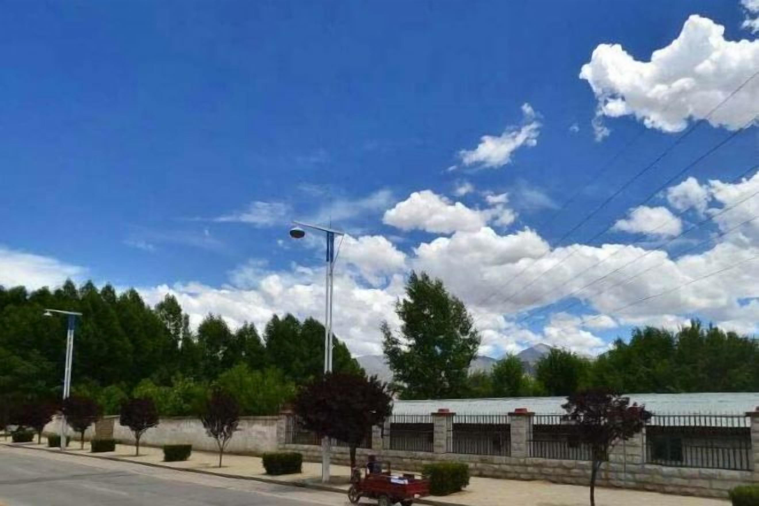 A clear sky with clouds, a street with a parked car, and a building with a fence.