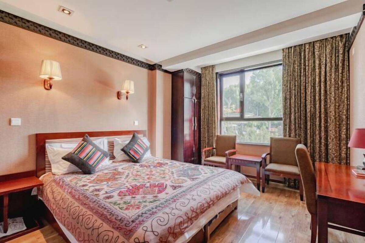 Een hotelkamer met een groot bed, twee bedlampjes, een houten bureau en een raam met gordijnen.