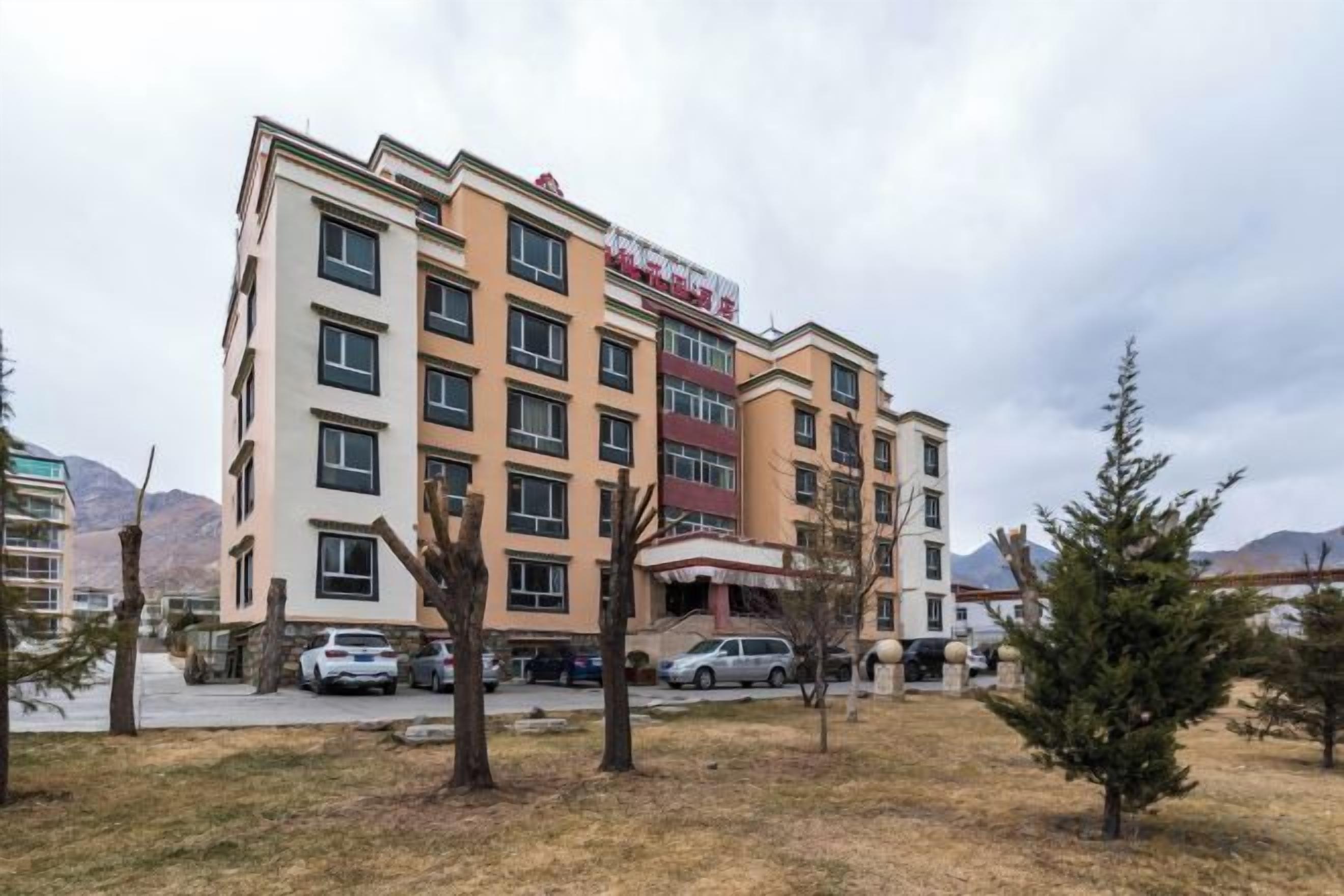 Un hotel de varios pisos con techo plano, varias ventanas y un estacionamiento con automóviles.