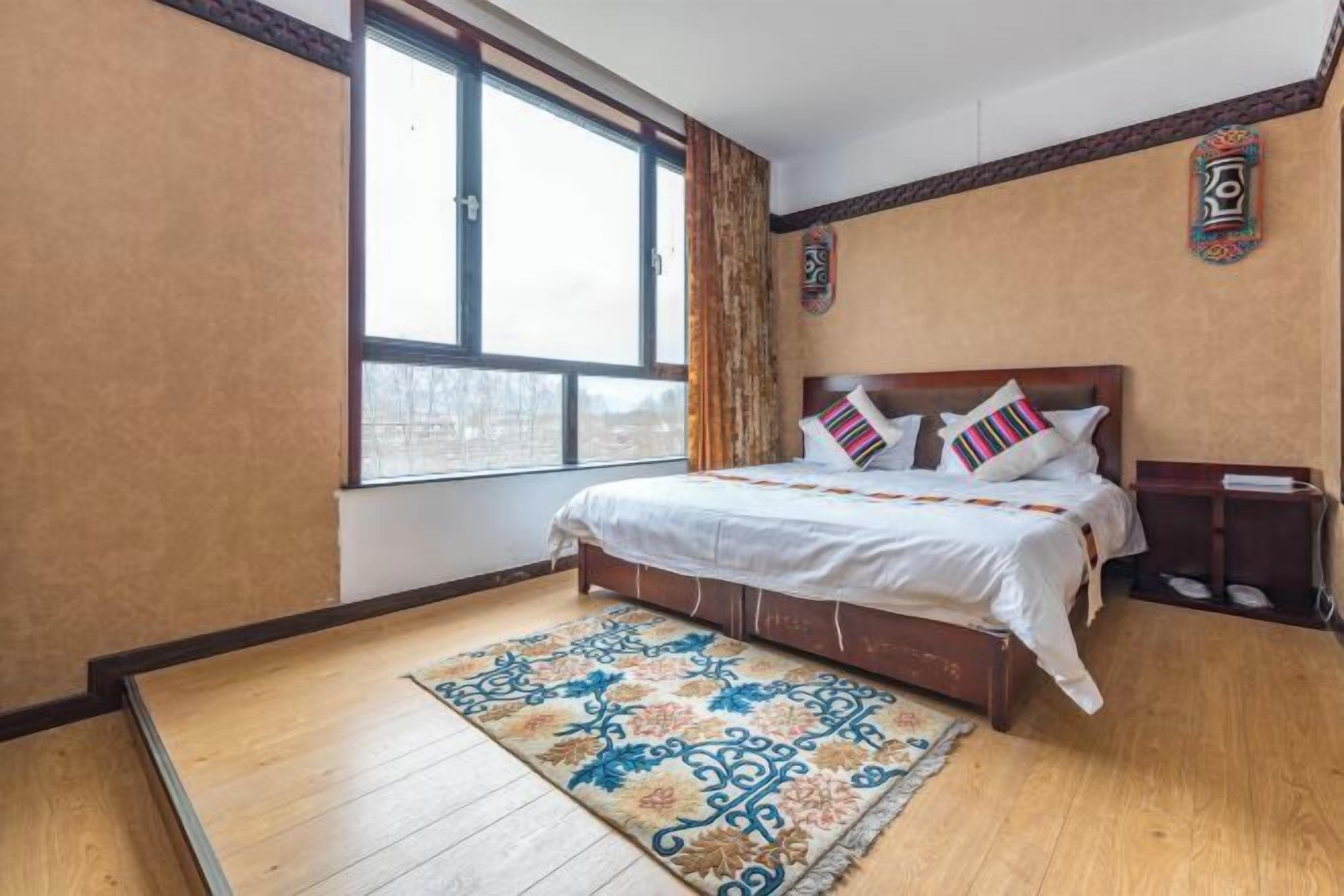 Un dormitorio con cama, ventana, suelo de madera y alfombra estampada.