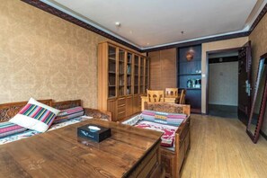 A room with a wooden sofa set, a dining table, a cabinet with glass doors, and a small wooden chair. - Padma Chumig Garden Hotel (Lhasa)