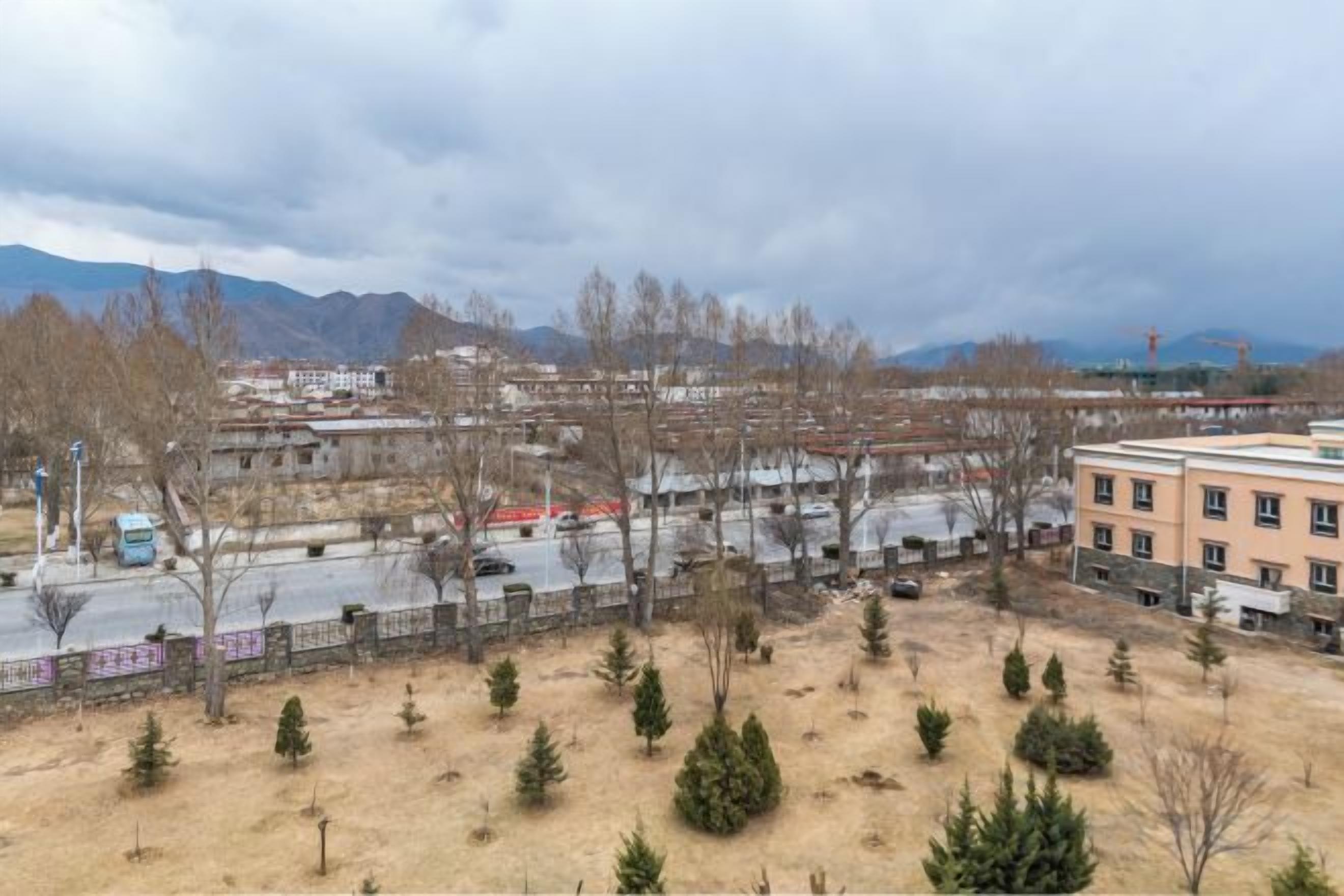 Vista di un complesso edilizio con diverse strutture, un'area di parcheggio e un'area recintata con alberi.