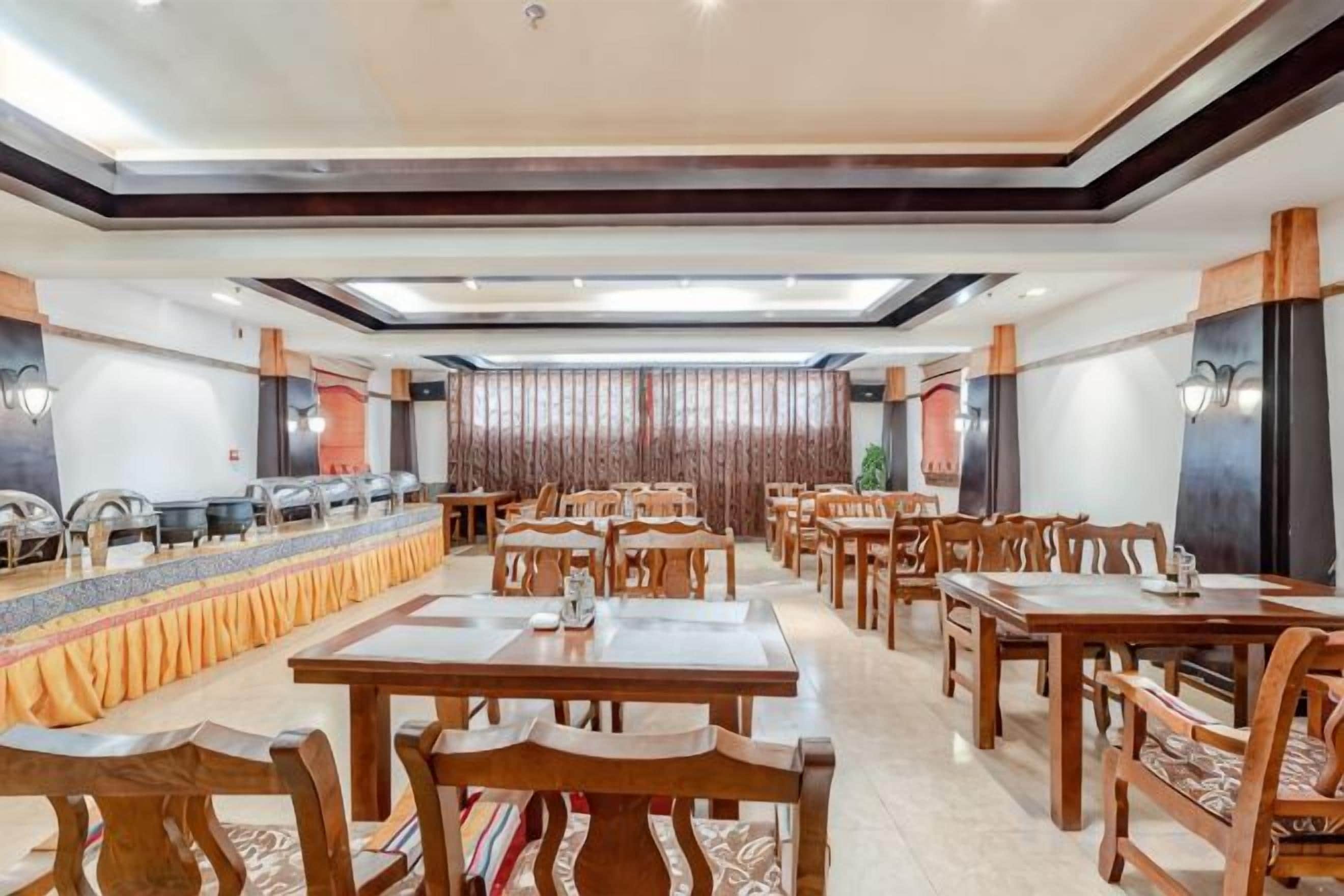 A spacious dining area with multiple tables and chairs, a long counter with a patterned tablecloth, and a modern ceiling design.