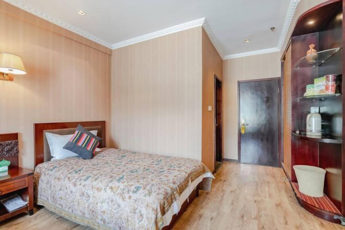 Een hotelkamer met een bed, nachtkastje, lamp, kast en een deur.