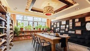 A library with bookshelves, a dining table, chairs, potted plants, and framed pictures on the walls. - Padma Chumig Garden Hotel (Lhasa)