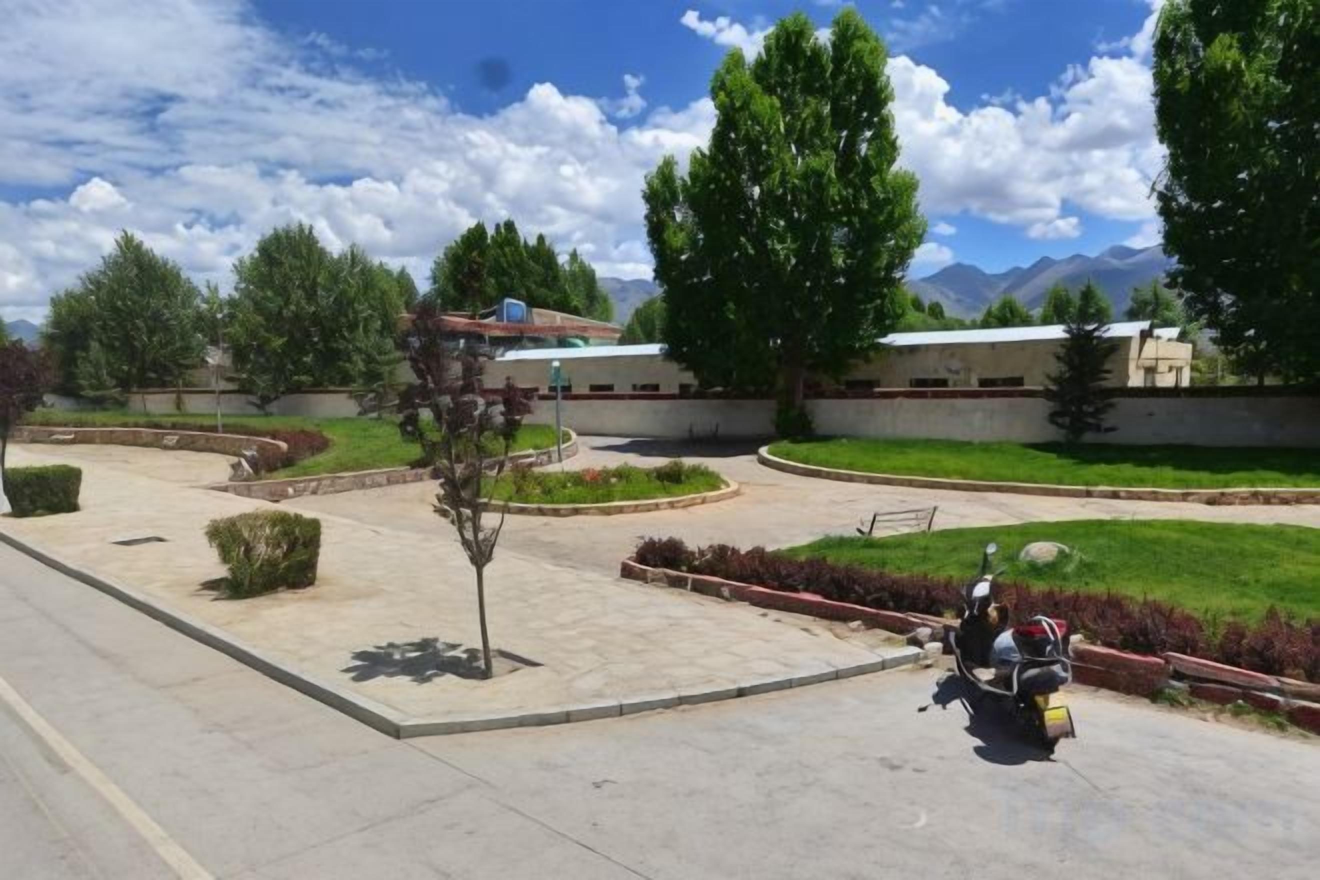 Un patio empedrado con una motocicleta, un edificio de techo plano y montañas al fondo.