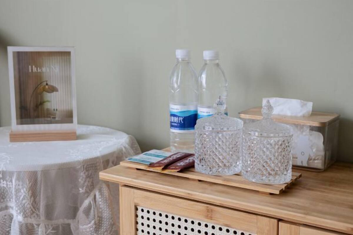 Uma mesa com toalha rendada, duas garrafas de água, uma caixa de lenços e um objeto decorativo.