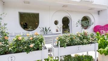 A white building with multiple windows, a balcony with plants, and a pink heart-shaped decoration.