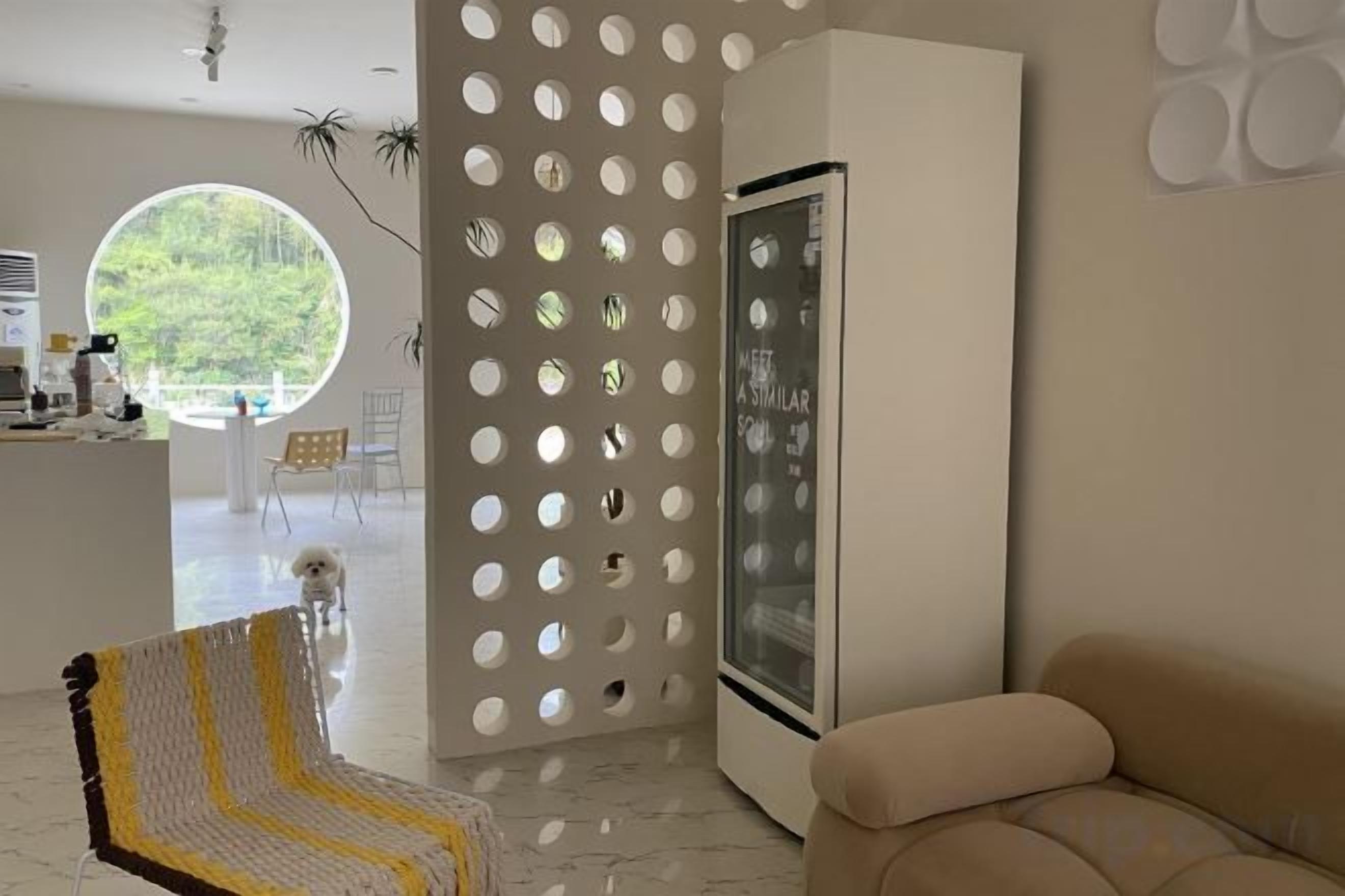 Una sala moderna con sofá, una silla estampada, una zona de cocina y un ventanal grande.