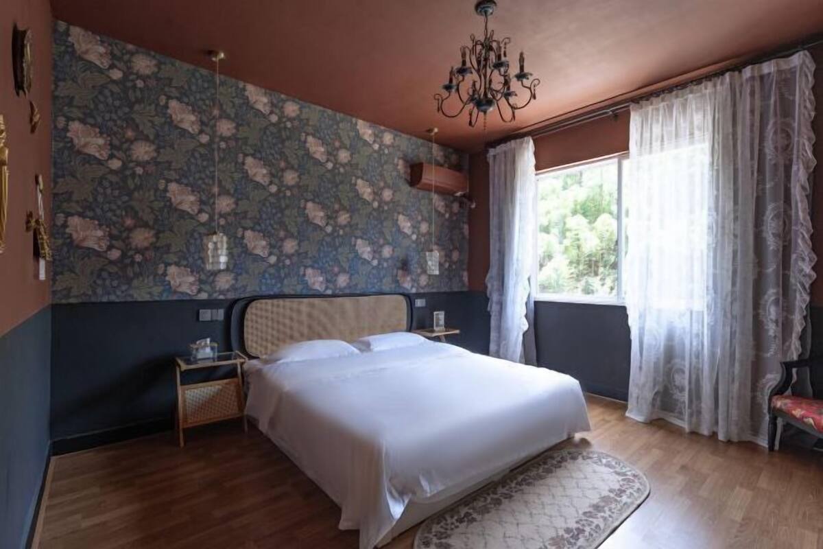 Quarto com cama, lustre, janela com cortinas e parede estampada.