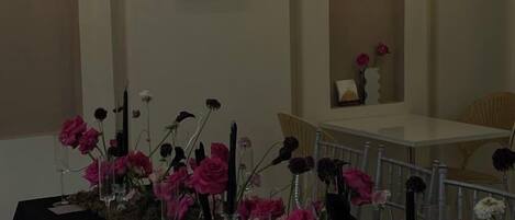 A table set with pink flowers and candles, a white tablecloth, and a vase with a single flower.