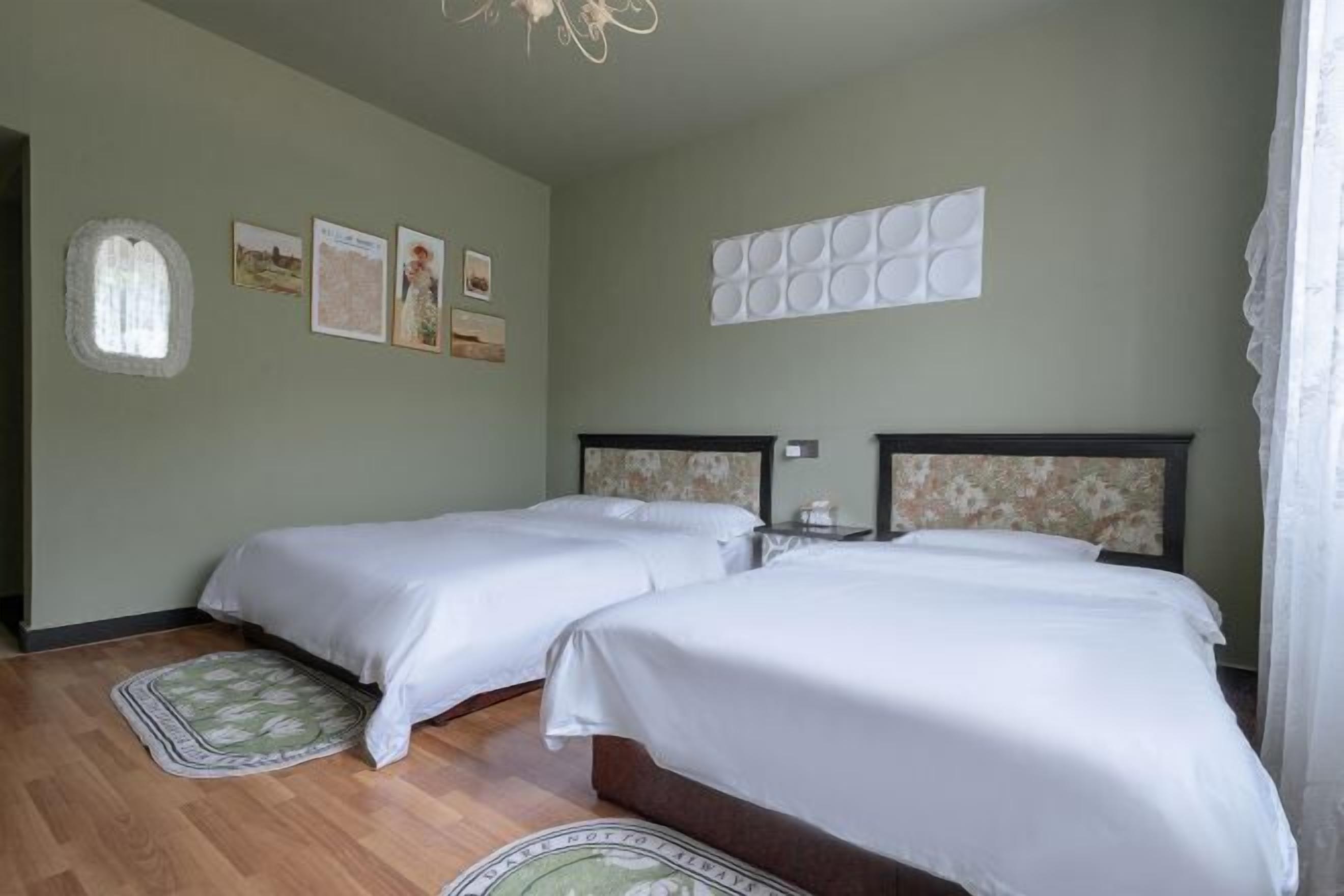 A room with two beds, a small table, a wall-mounted light, and a window with a view.