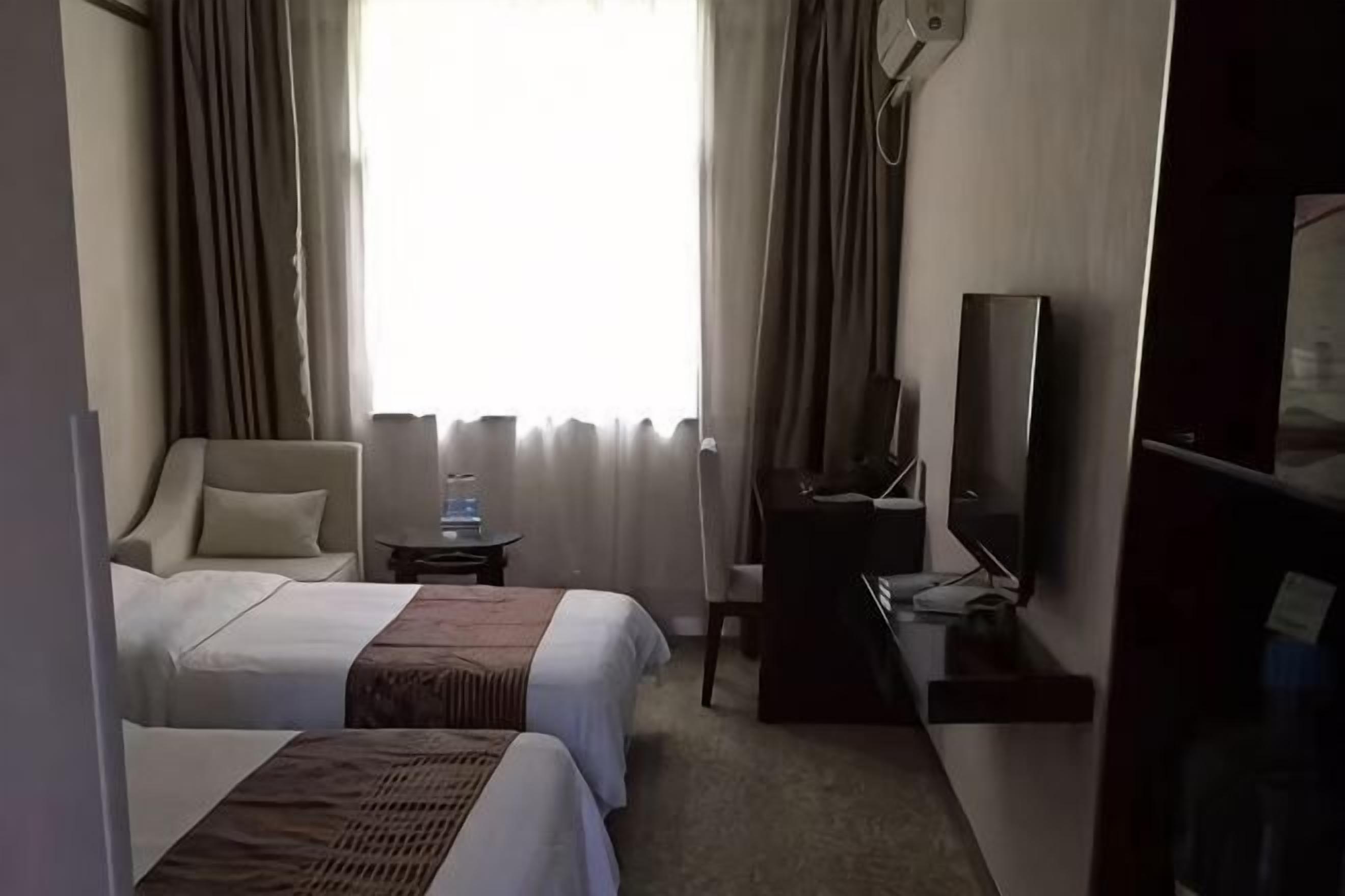 Habitación de hotel con dos camas, un escritorio, una silla, un televisor y un ventanal con cortinas.
