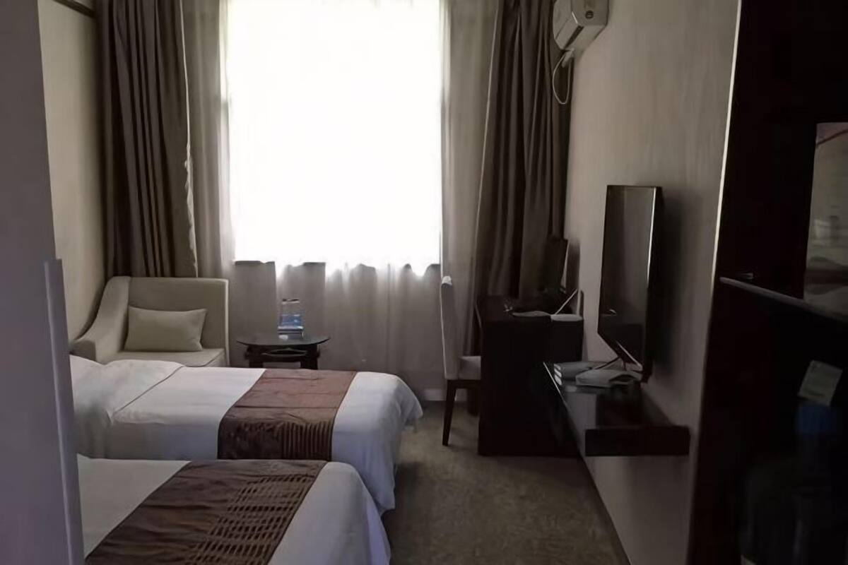 A hotel room with two beds, a desk, a chair, a TV, and a window with curtains.