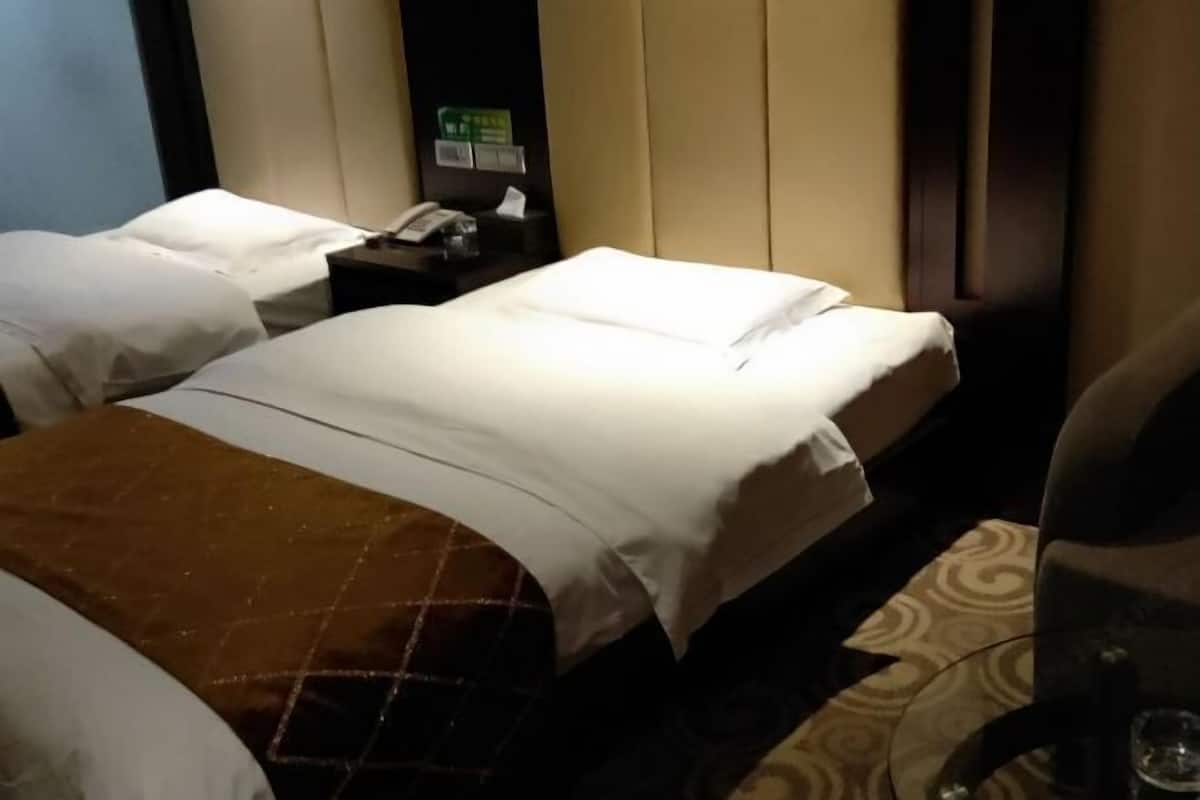Ein Hotelzimmer mit zwei Betten, einem Nachttisch mit Telefon und einem grünen Schild, sowie einem Glastisch mit einem Glas.