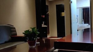 Ein Hotelrezeptionstresen mit einem Blumentopf, einem schwarzen Stuhl und einem Spiegel, der ein Badezimmer mit Waschbecken und Fenster zeigt.