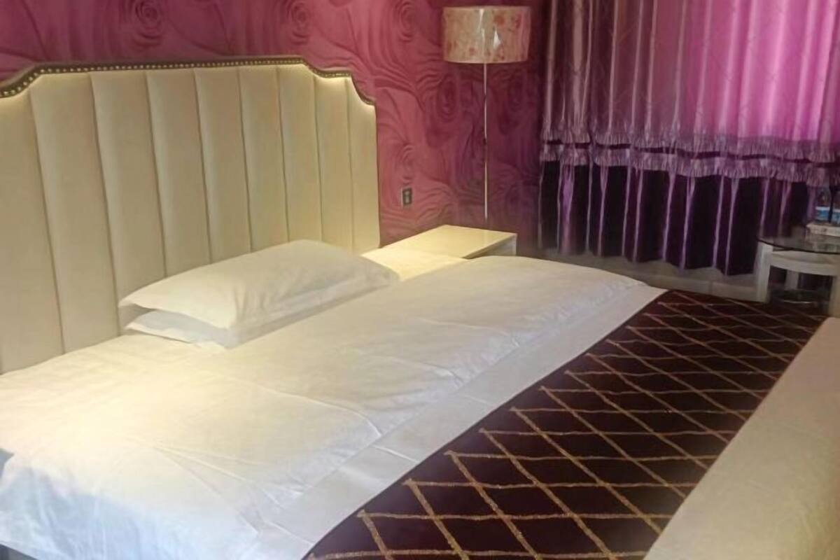 Ein Hotelzimmer mit Bett, Nachttisch, Lampe und einem Fenster mit Vorhängen.