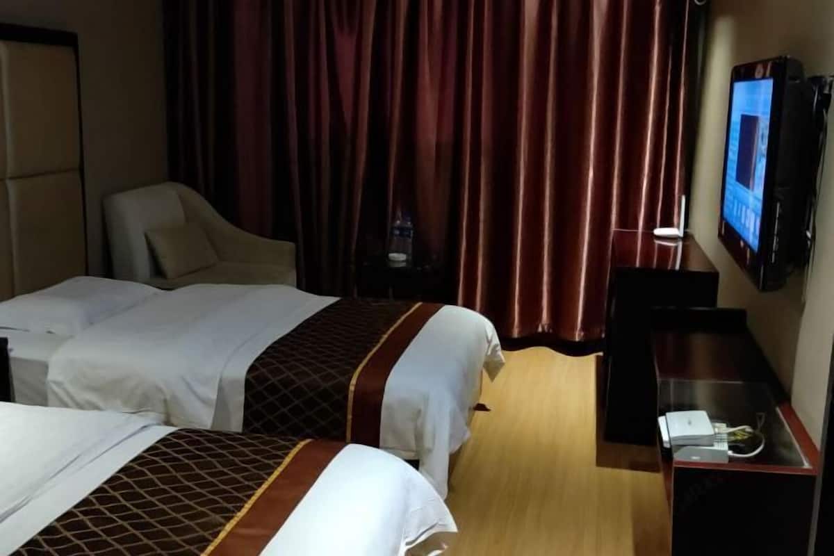 Ein Hotelzimmer mit zwei Betten, einem Schreibtisch, einem Stuhl, einem Fernseher und einem Vorhang.