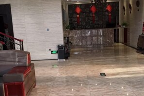 Un hall d’hôtel comprenant un comptoir d’accueil, un espace détente avec un canapé et un sol en marbre.